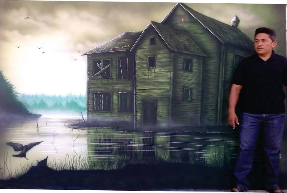 Mural de uma casa em cenário sombrio, com o artista ao lado.